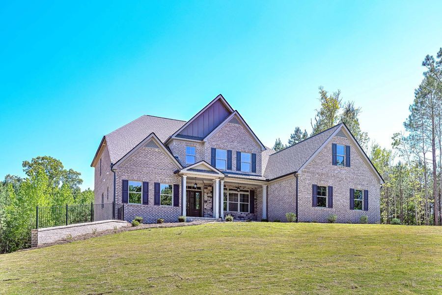 Two-story brick house with blue shutters, set on a grassy hill against a blue sky and trees.