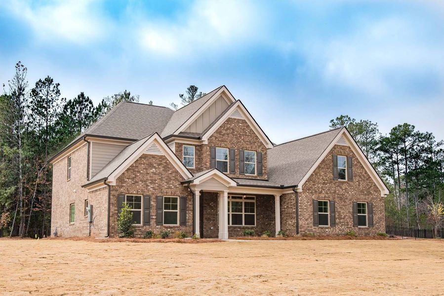 Two-story brick house with beige trim and brown roof against a cloudy sky and sparse foliage.