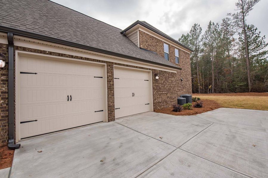 Two-car garage with tan doors, brick exterior, and concrete driveway.