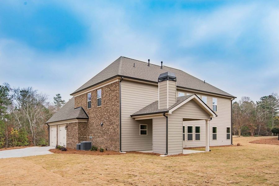 Two-story house with brick and siding, driveway, chimney, and grassy yard under a cloudy sky.