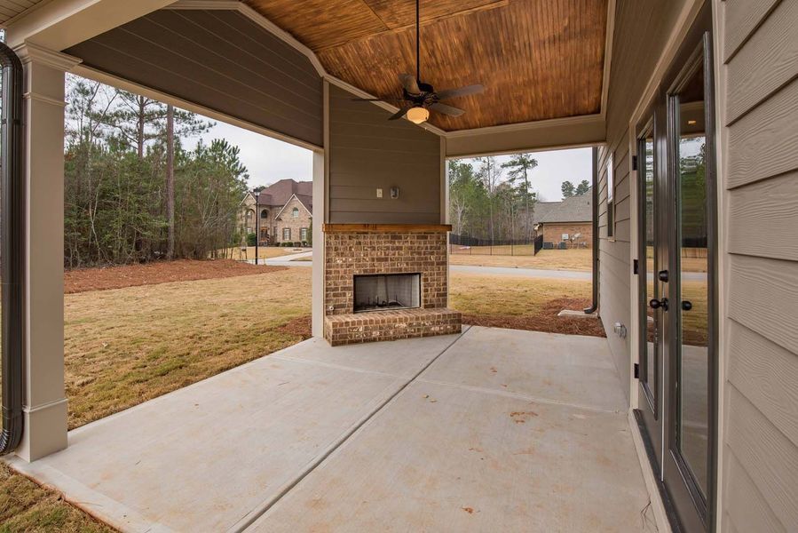 Covered patio with a brick fireplace, concrete floor, and a tan ceiling with a ceiling fan.