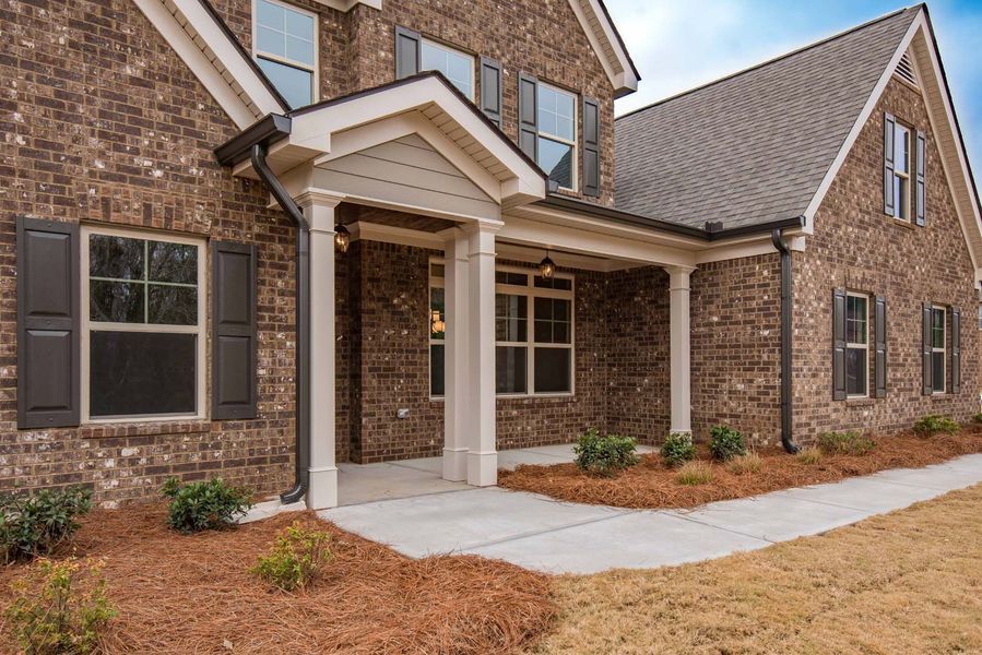 Brick house with covered porch, gray shutters, and brown landscaping on a sunny day.