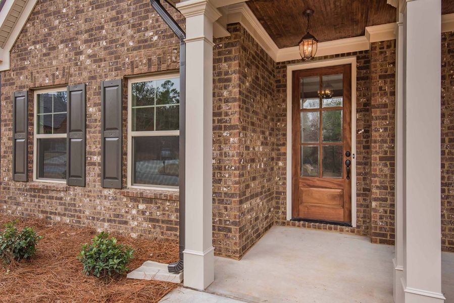 Brick house exterior with a wooden door, windows, and white columns.