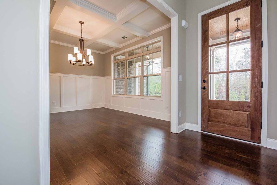 Empty dining room with dark wood floor, wooden door, and light fixture.