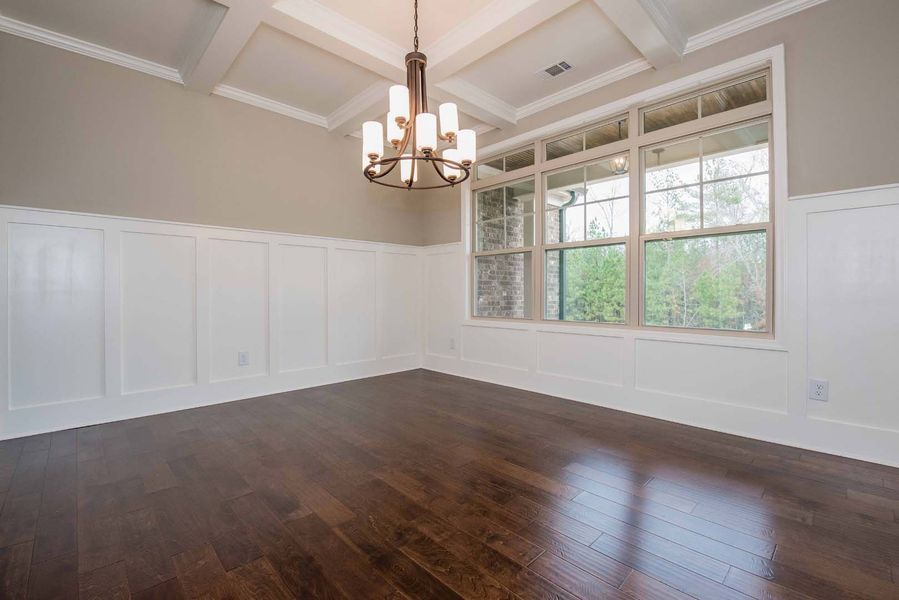 Empty dining room with dark wood floors, white wainscoting, gray walls, and a chandelier.