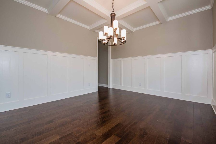 Empty dining room with dark wood floors, white wainscoting, and a chandelier.