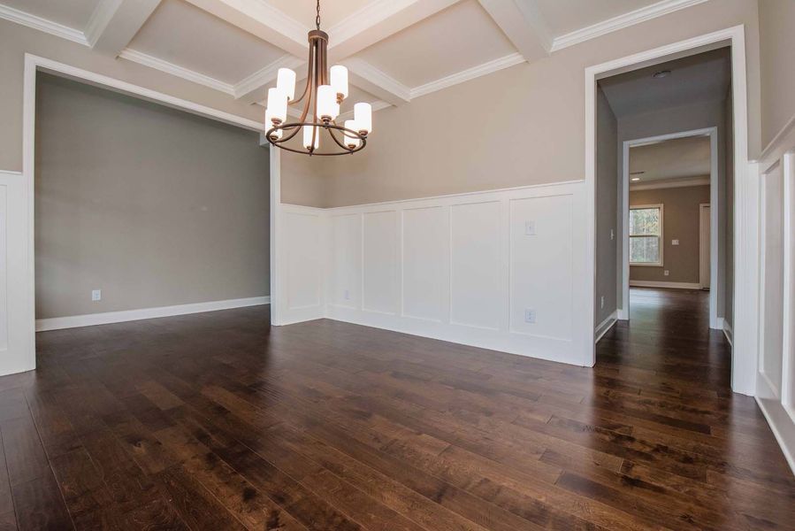Empty dining room with dark wood floors, white wainscoting, and a chandelier.