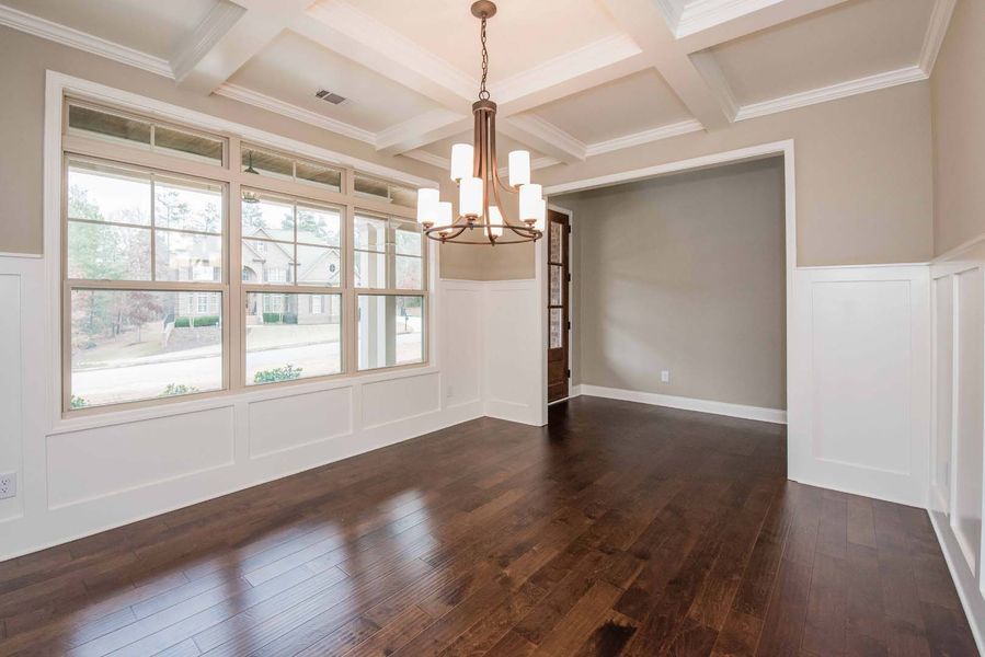 Dining room with dark wood floors, large windows, chandelier, and white wainscoting.