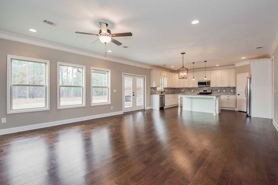 Spacious living area with dark wood floors, cream walls, and a kitchen.
