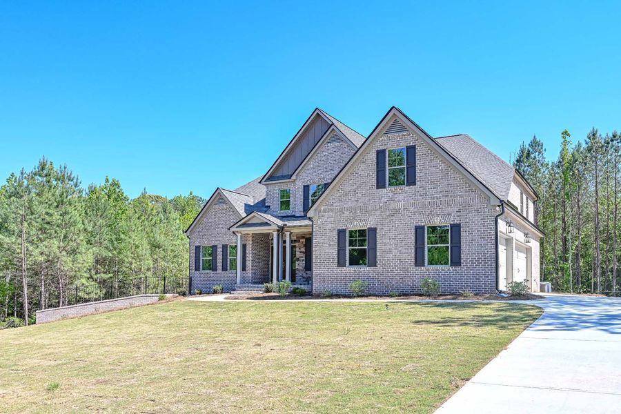 Two-story brick home with a porch, shutters, and a driveway, set in a grassy area with trees under a blue sky.