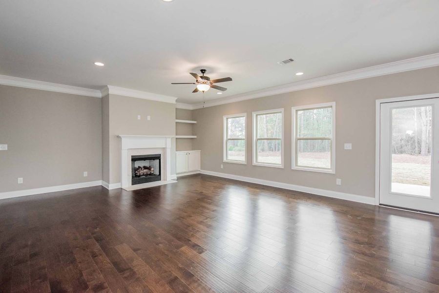Empty living room with hardwood floors, fireplace, and windows.