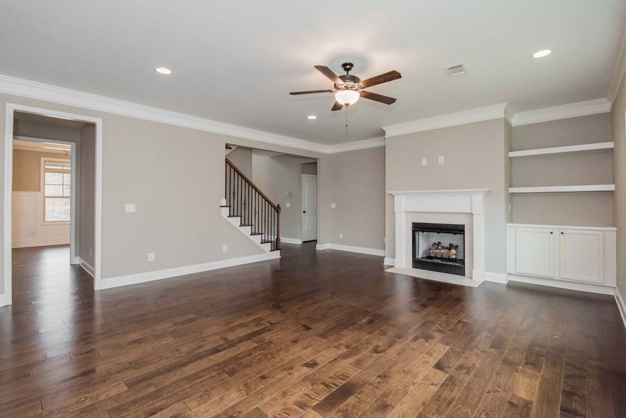 Empty living room with dark wood floors, fireplace, and built-in shelves.