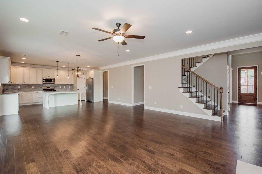 Spacious open-concept living area with kitchen, staircase, and dark wood flooring.