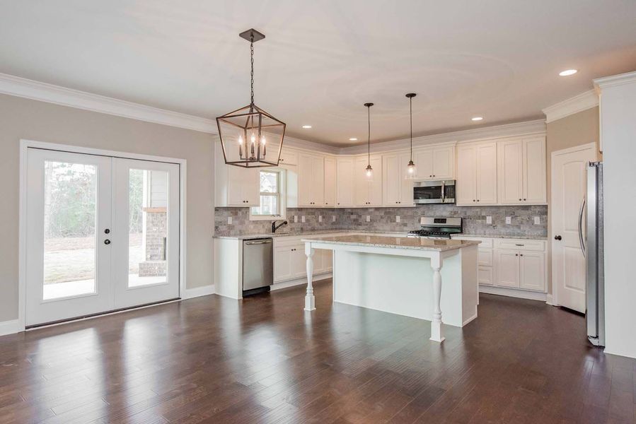 Spacious kitchen with white cabinets, island, and dark wood floors. A large window and french doors