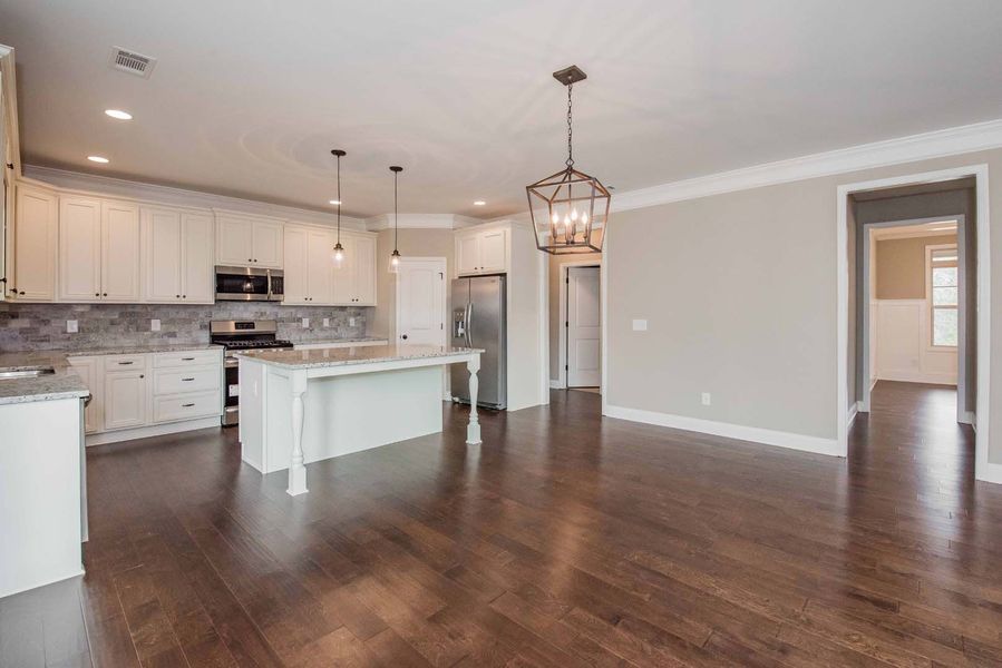 Spacious kitchen with white cabinets, island, stainless steel appliances, and dark wood floors.