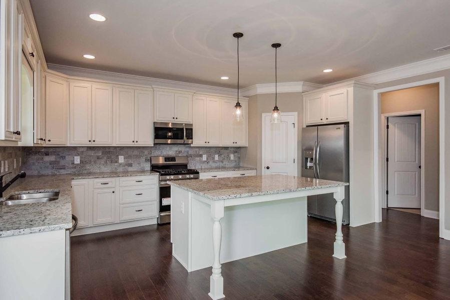 Bright kitchen with white cabinets, granite counters, island with pendant lights, and stainless steel appliances.