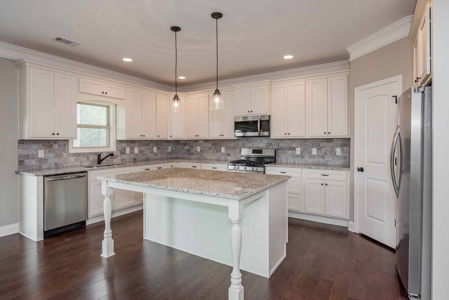 White kitchen with island, stainless steel appliances, dark wood floor, and gray tile backsplash.