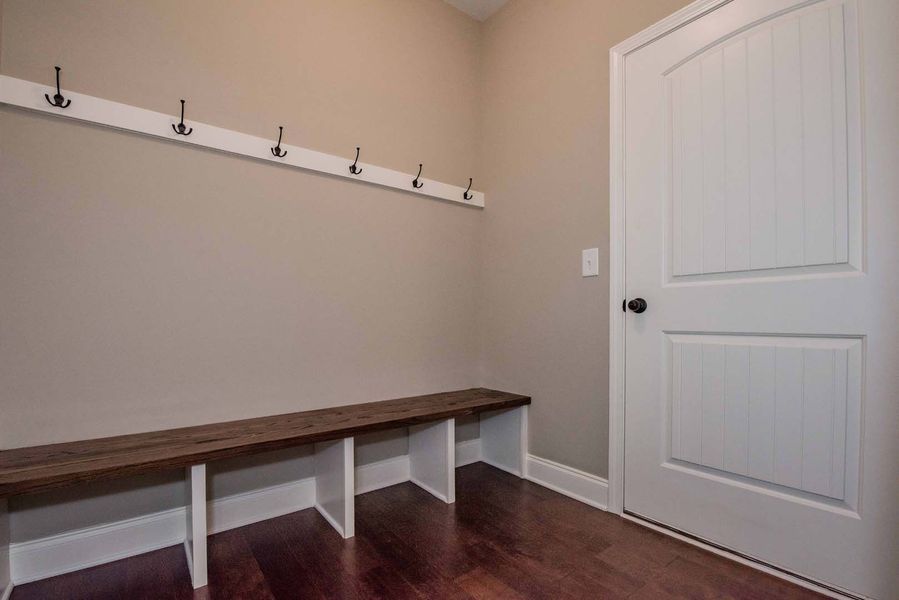 A small entryway with a bench and hooks on the wall. A white door is on the right.