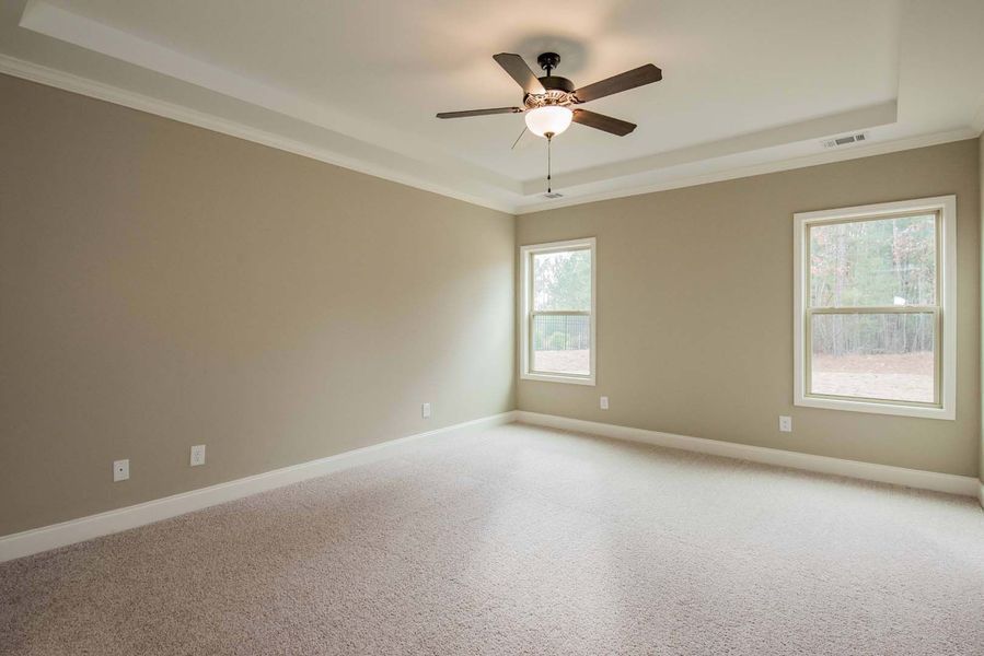 Empty beige bedroom with carpet, ceiling fan, and two windows.