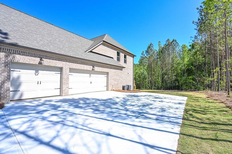 Two-car garage with white doors, brick facade, and concrete driveway. Tall trees and blue sky in background.