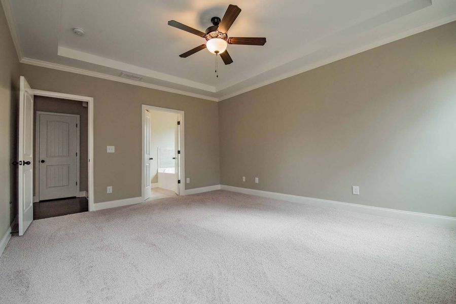 Empty beige bedroom with a ceiling fan and two doors.