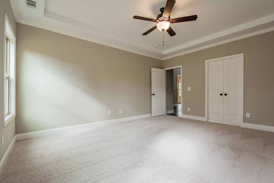 Empty bedroom with beige walls, white trim, and carpet; a closet and a doorway.