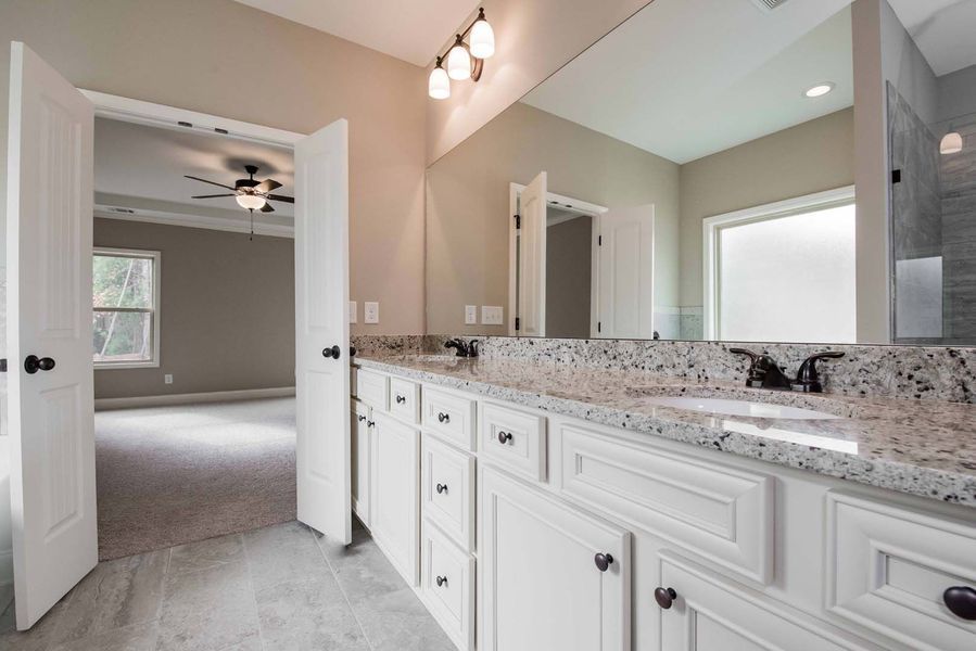 Bathroom with a white vanity, granite countertop, large mirror, and doors leading to a bedroom.