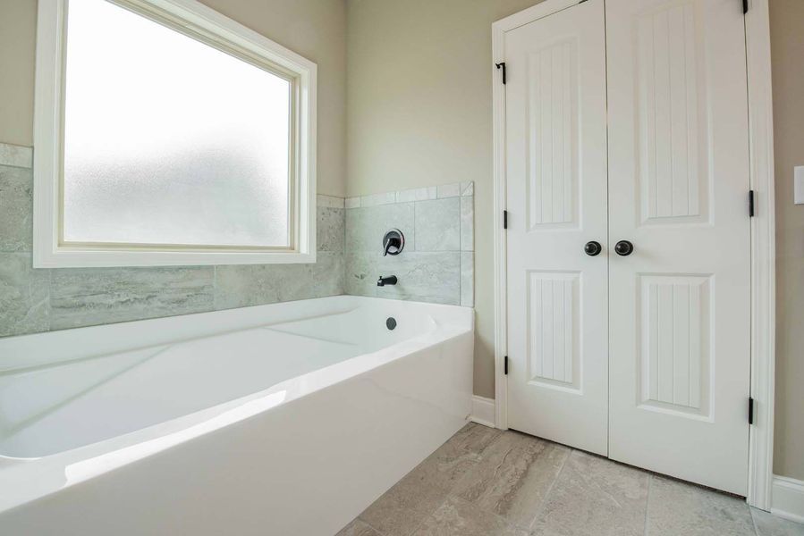 Modern bathroom with white tub, frosted window, tile wall, and white double doors.