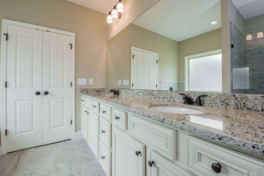 Bathroom with white cabinets, granite countertop, large mirror, and a shower.