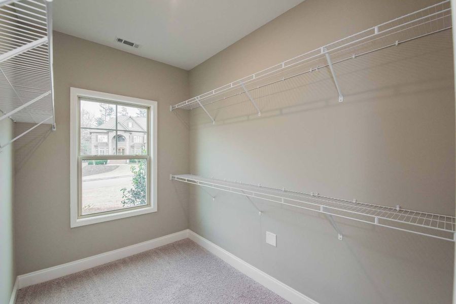 Empty walk-in closet with wire shelving, window, and carpeted floor; neutral paint.