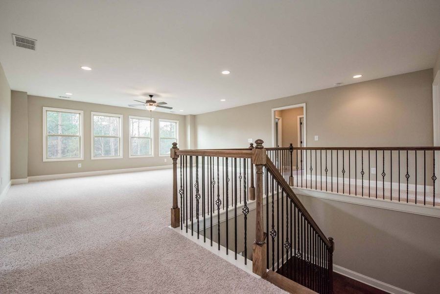 Empty room with staircase, beige carpet, walls, and ceiling. Windows on the left.