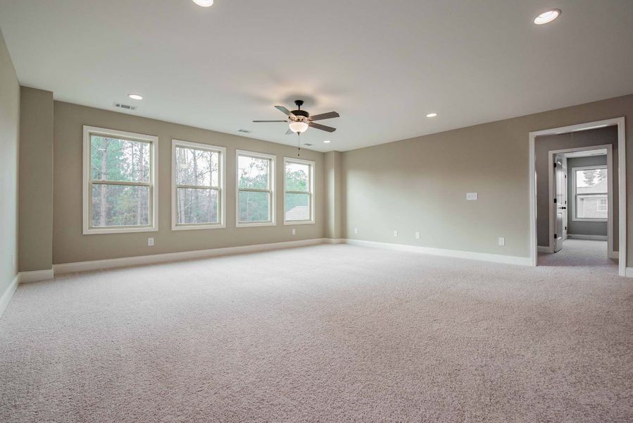Empty room with neutral carpet and walls, windows, and a ceiling fan.