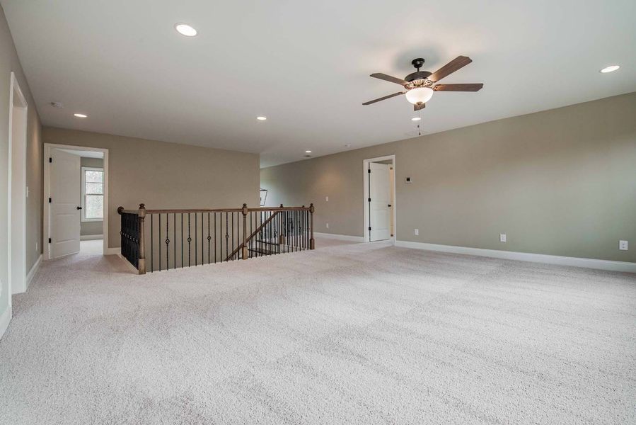 Spacious, carpeted upstairs landing with staircase, ceiling fan, and neutral-colored walls.