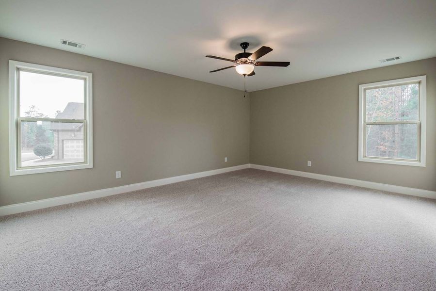 Empty bedroom with gray walls, carpet, two windows, and a ceiling fan.