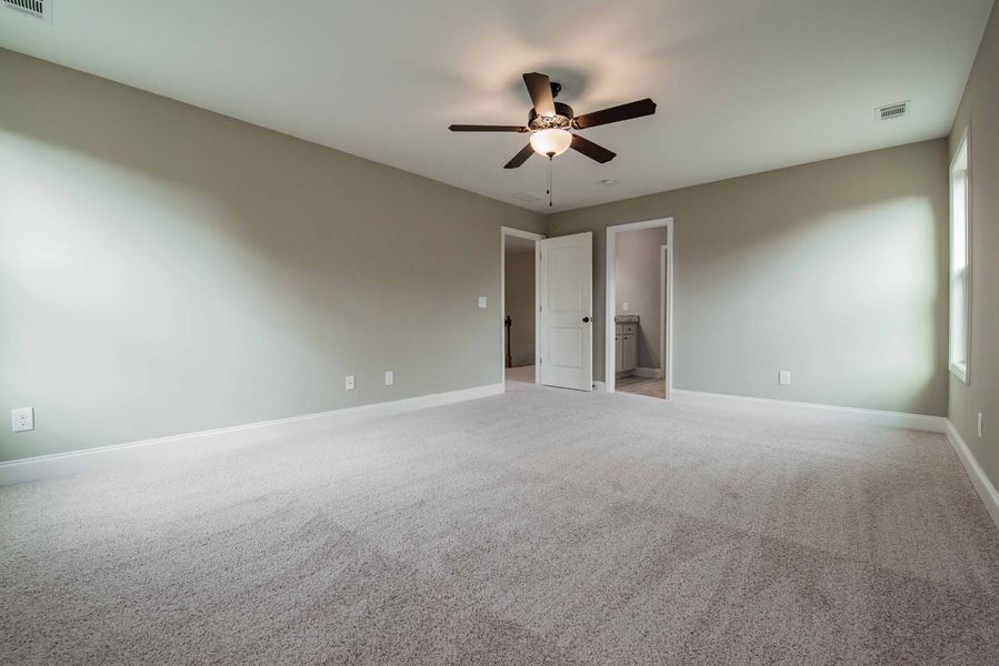 Empty room with gray carpet, walls, and ceiling fan, featuring two doors and a window.