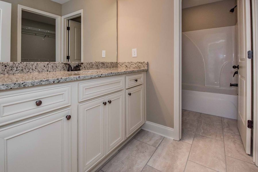 Bathroom with white cabinets, granite countertop, and a tub.