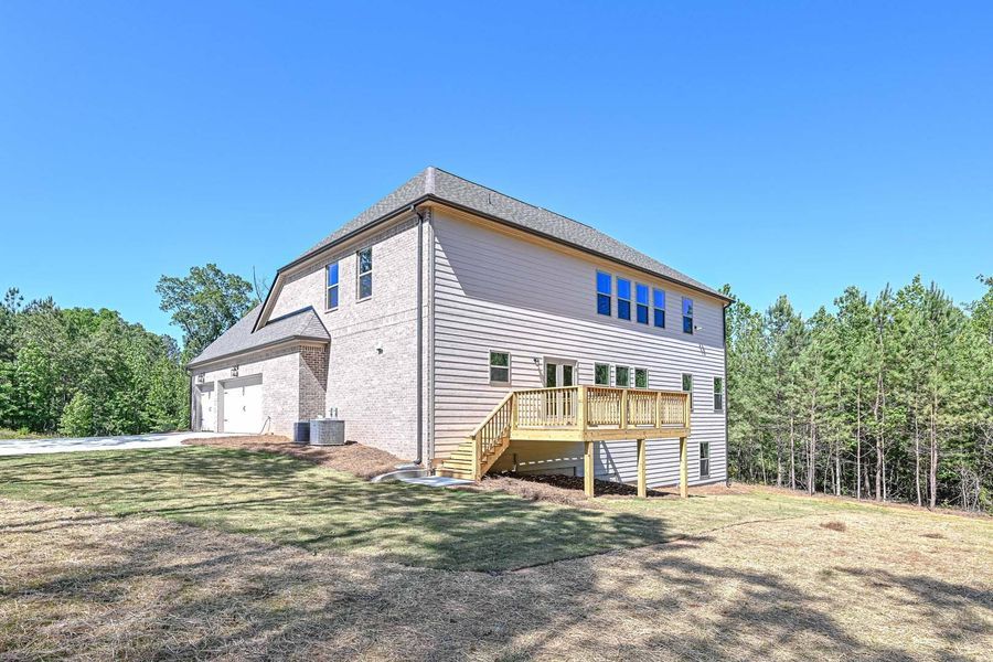 Two-story brick house with a wooden deck, garage, and surrounded by trees under a blue sky.