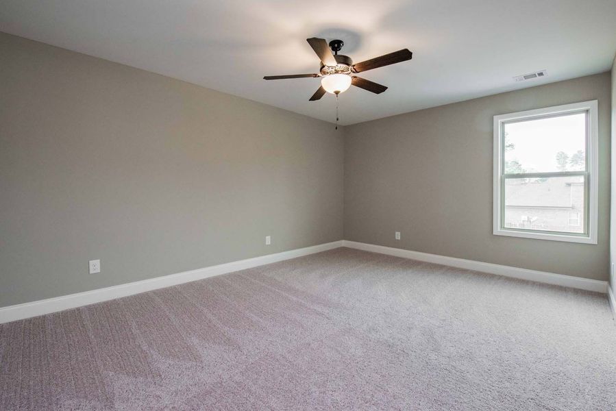 Empty bedroom with gray walls, light carpet, ceiling fan, and a window.
