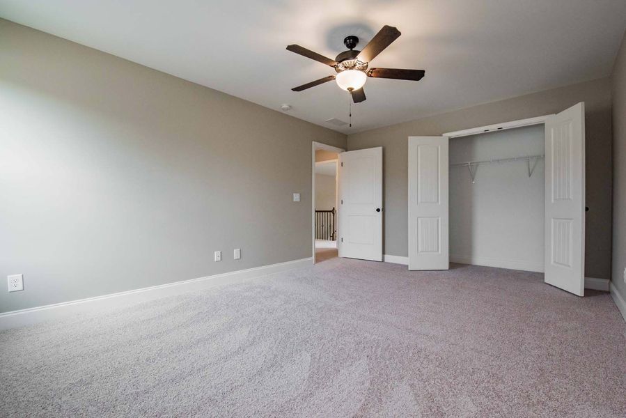 Empty bedroom with gray walls, carpet, and a ceiling fan. Closet doors are open.
