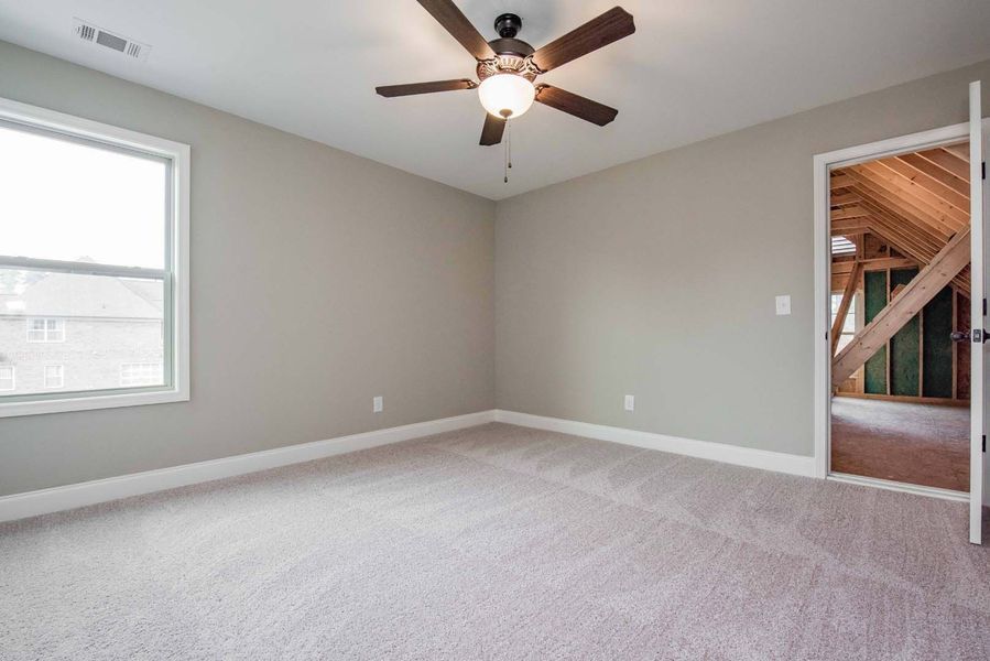 Empty bedroom with neutral walls, carpet, ceiling fan, and doorway to attic.