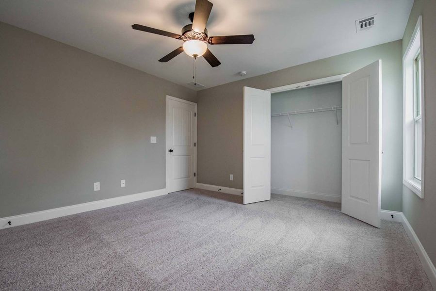 Empty bedroom with gray walls, white trim, carpet, and closet. Ceiling fan.