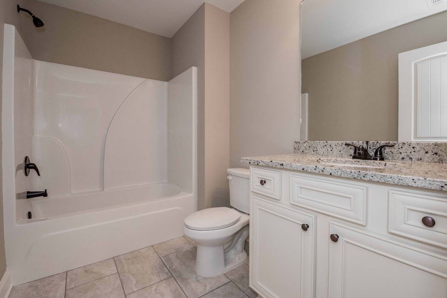 Bathroom with white tub/shower, toilet, vanity with granite countertop, and light gray walls.