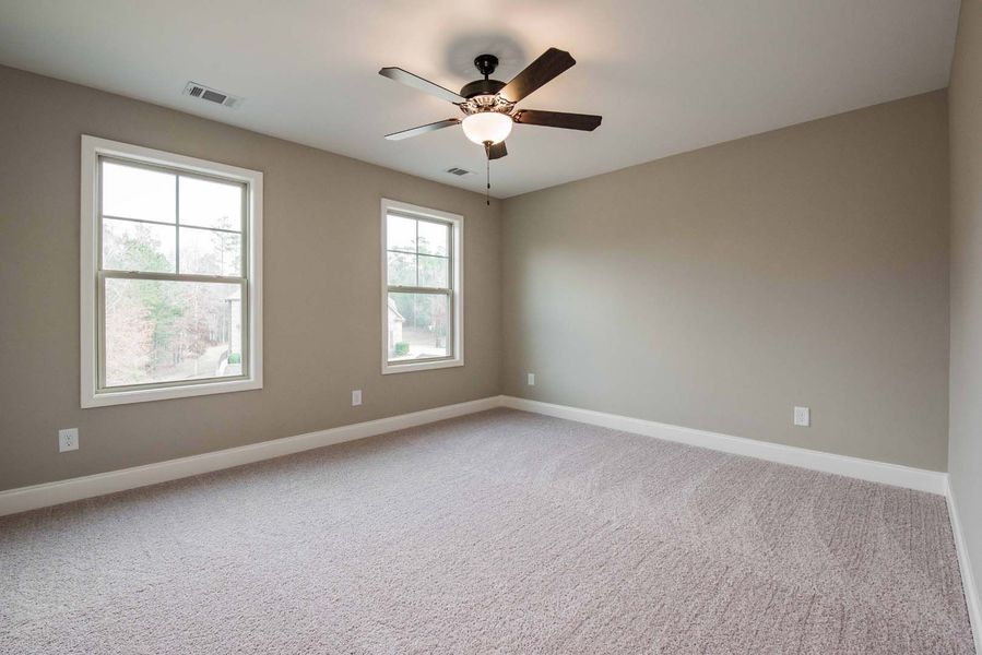 Empty bedroom with two windows, tan walls, carpet, and a ceiling fan.