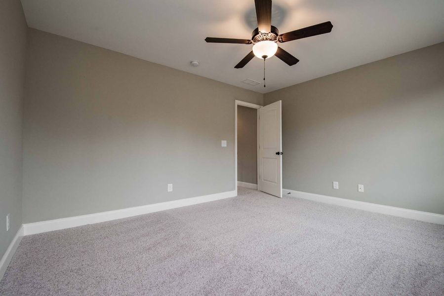 Empty bedroom with gray walls, white trim, and carpet. Ceiling fan and open white door.