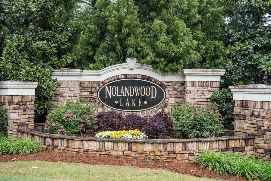 Nolandwood Lake entrance sign: stone facade, black oval sign with white lettering, surrounded by bushes and flowers.