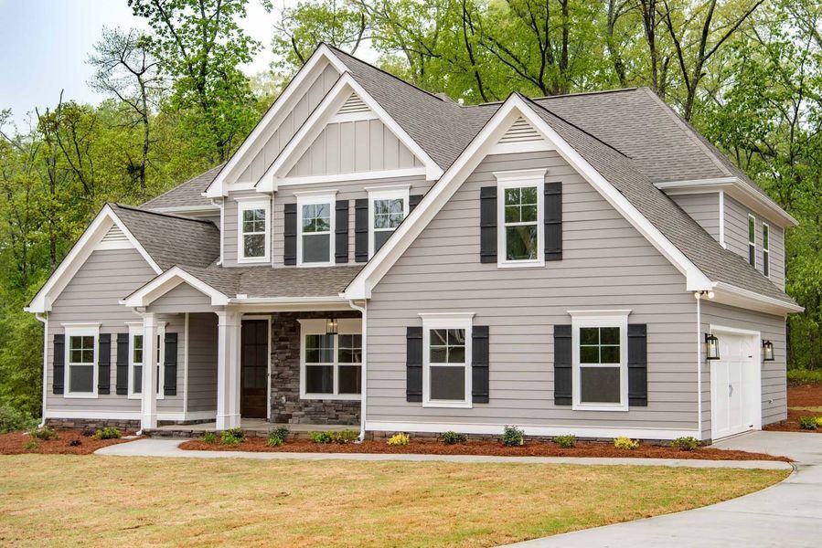 Two-story gray house with black shutters, brown roof, and a stone-covered entryway.