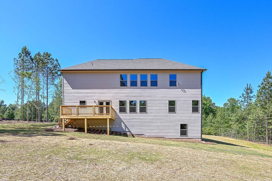Two-story beige house with a wooden deck, set against a blue sky and grassy landscape.