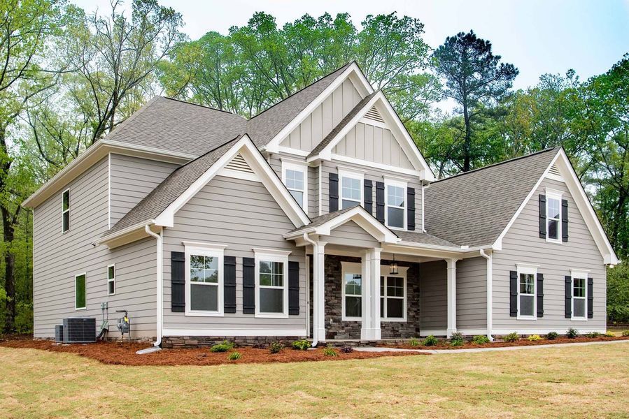 Two-story gray house with white trim, black shutters, and a front porch. Green trees in the background.