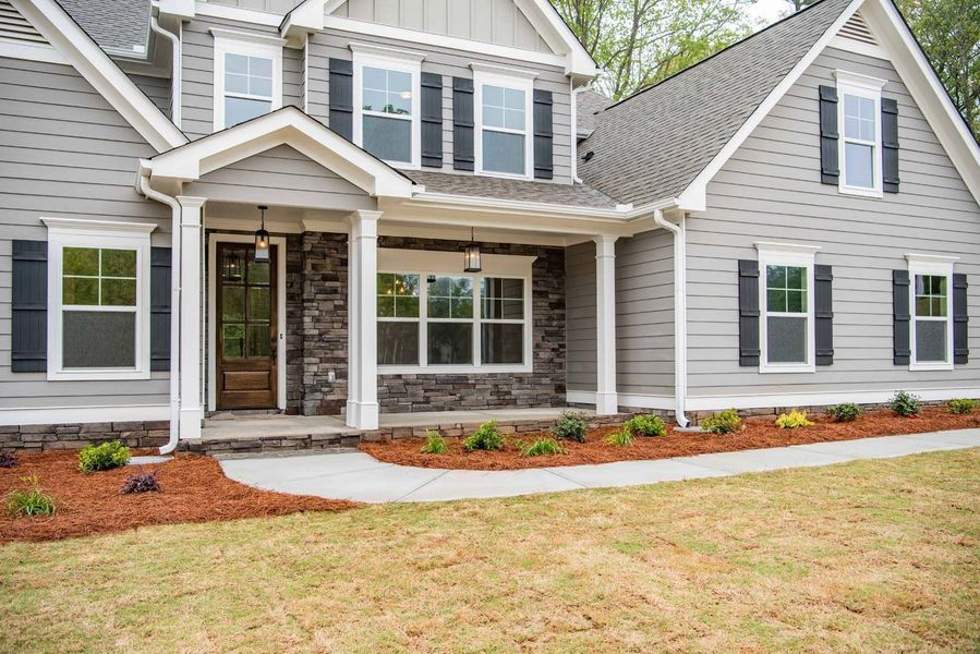 Gray two-story house with black shutters, a stone accent, and landscaping.