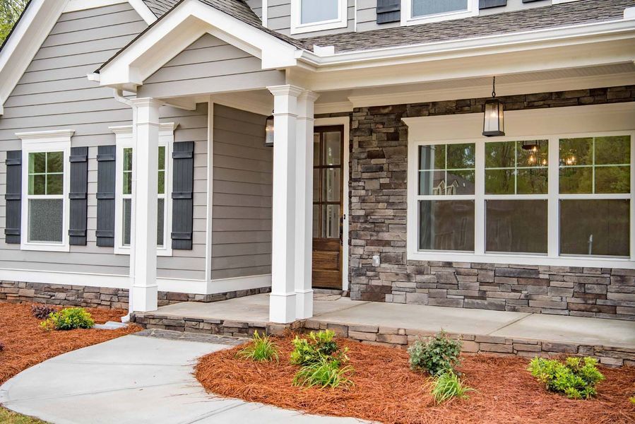 Gray house with stone accents, white trim, dark shutters, and a brown door.